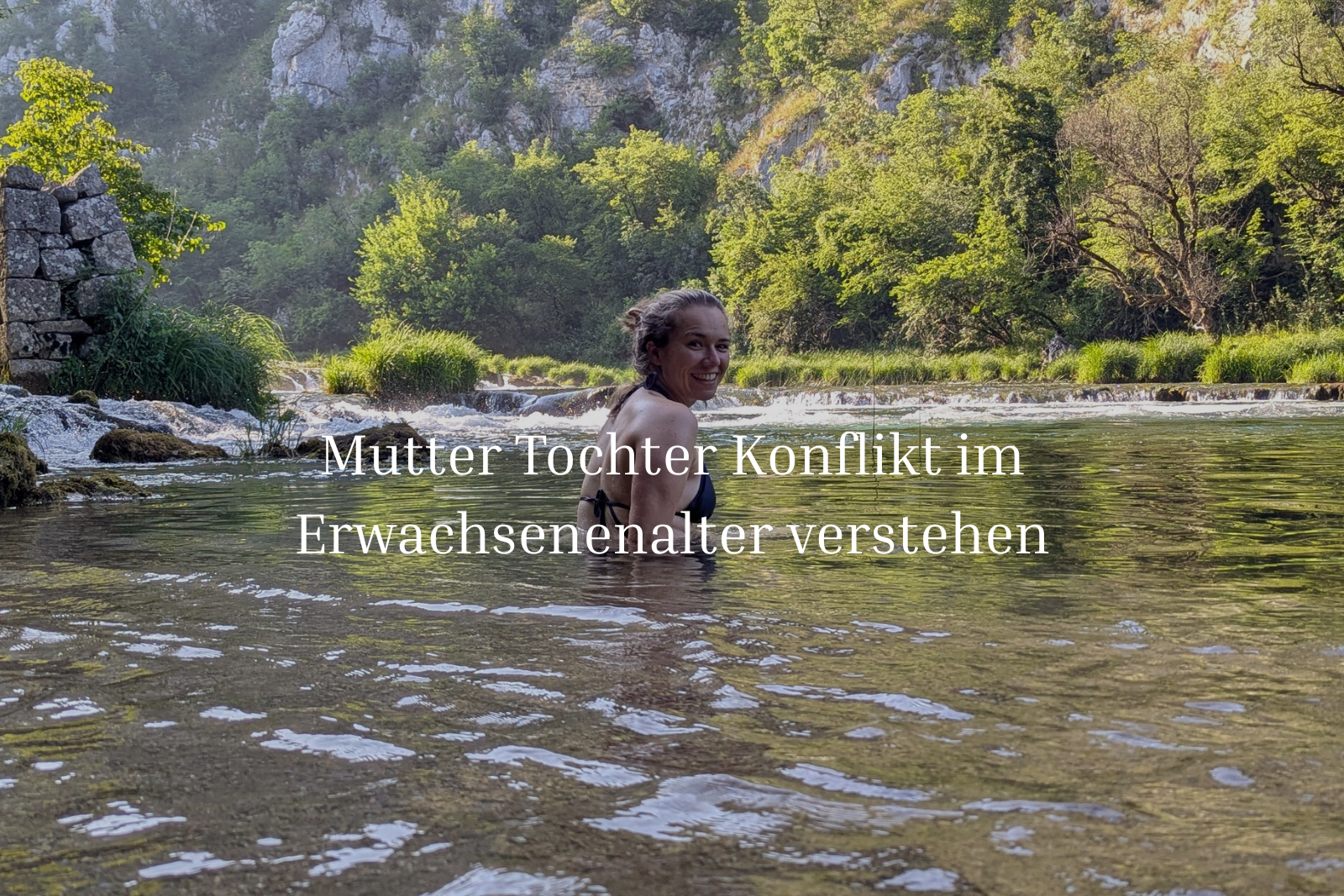 Johanna sitzt in einem See vor grünen Büschen.